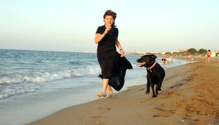 Η Ιωάννα Γκέρτσου σε νέα ηλικία, φορά ένα μαύρο φόρεμα και τρέχει δίπλα στη θάλασσα με το μαύρο λαμπραντόρ της